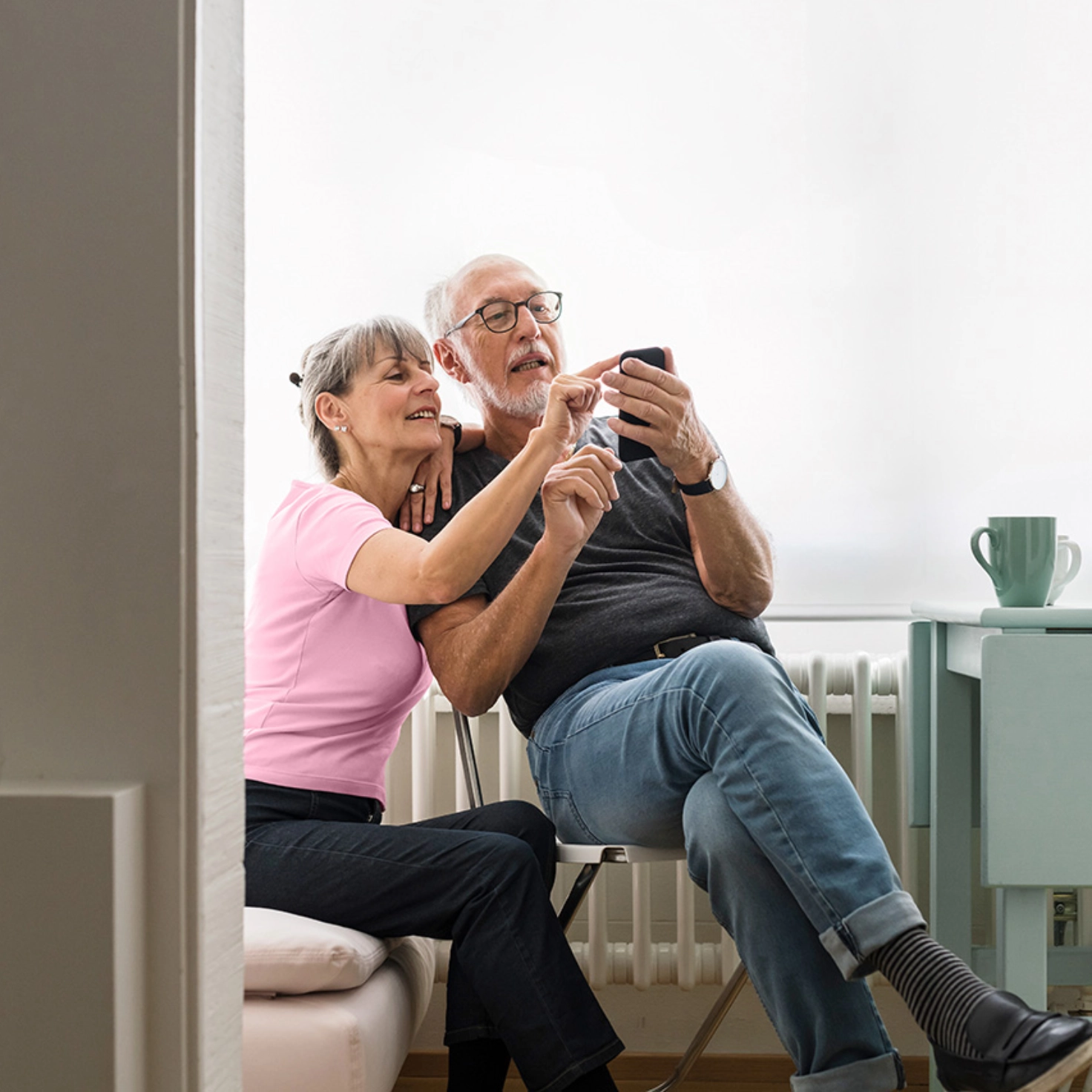 Ein älteres Paar sitzt im Wohnzimmer und tippt gemeinsam auf ein Handy.