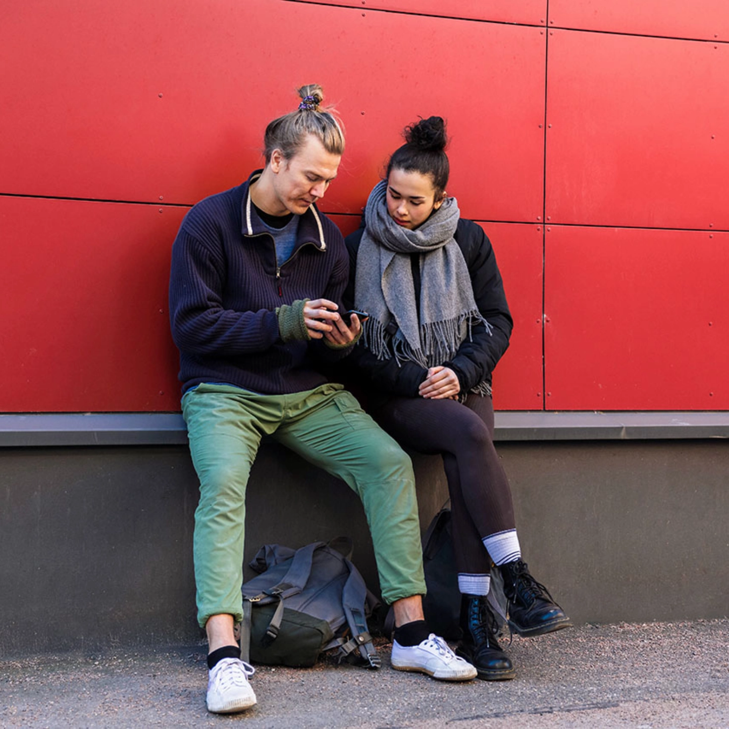 Ein Mann und eine Frau sitzen vor einem roten Gebäude und schauen gemeinsam auf sein Handy