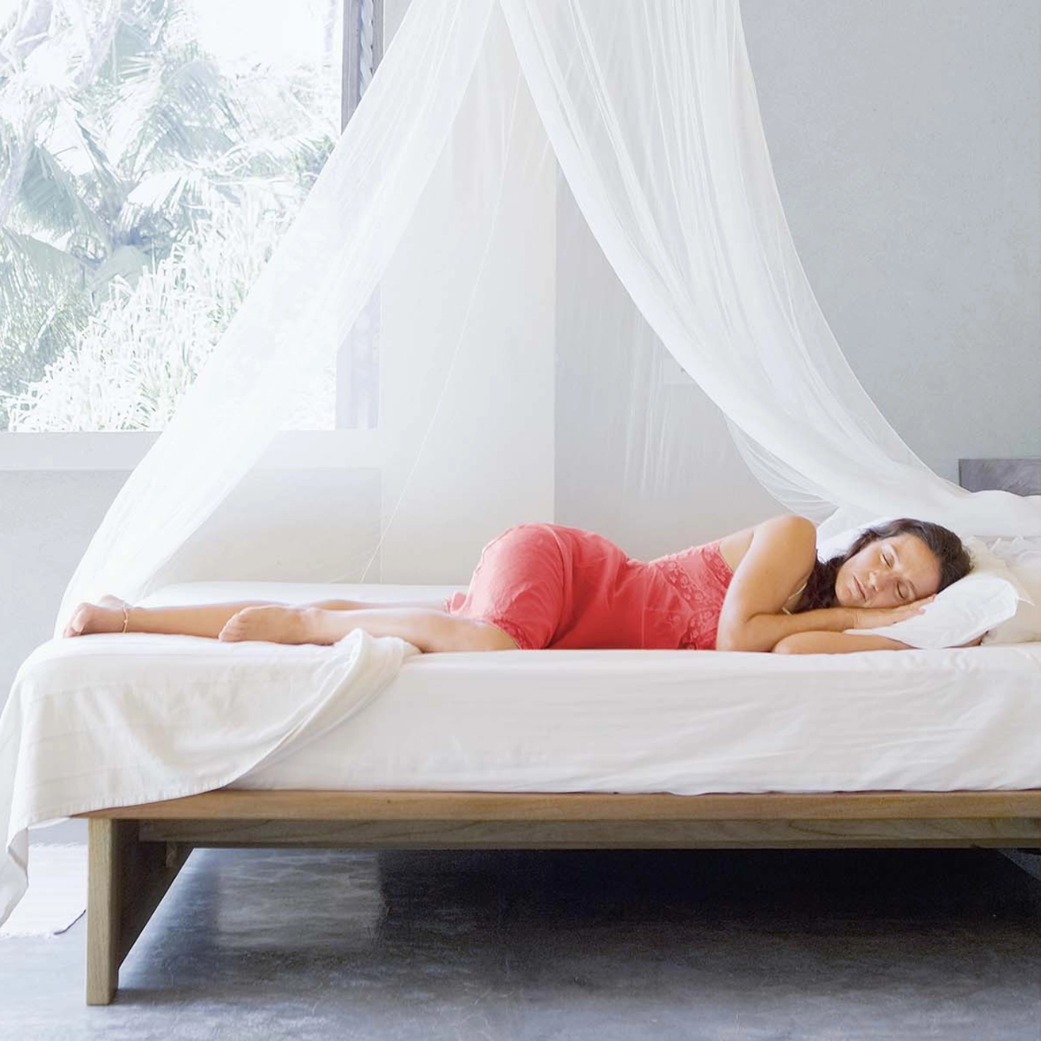 Une femme dort sous une moustiquaire en été.