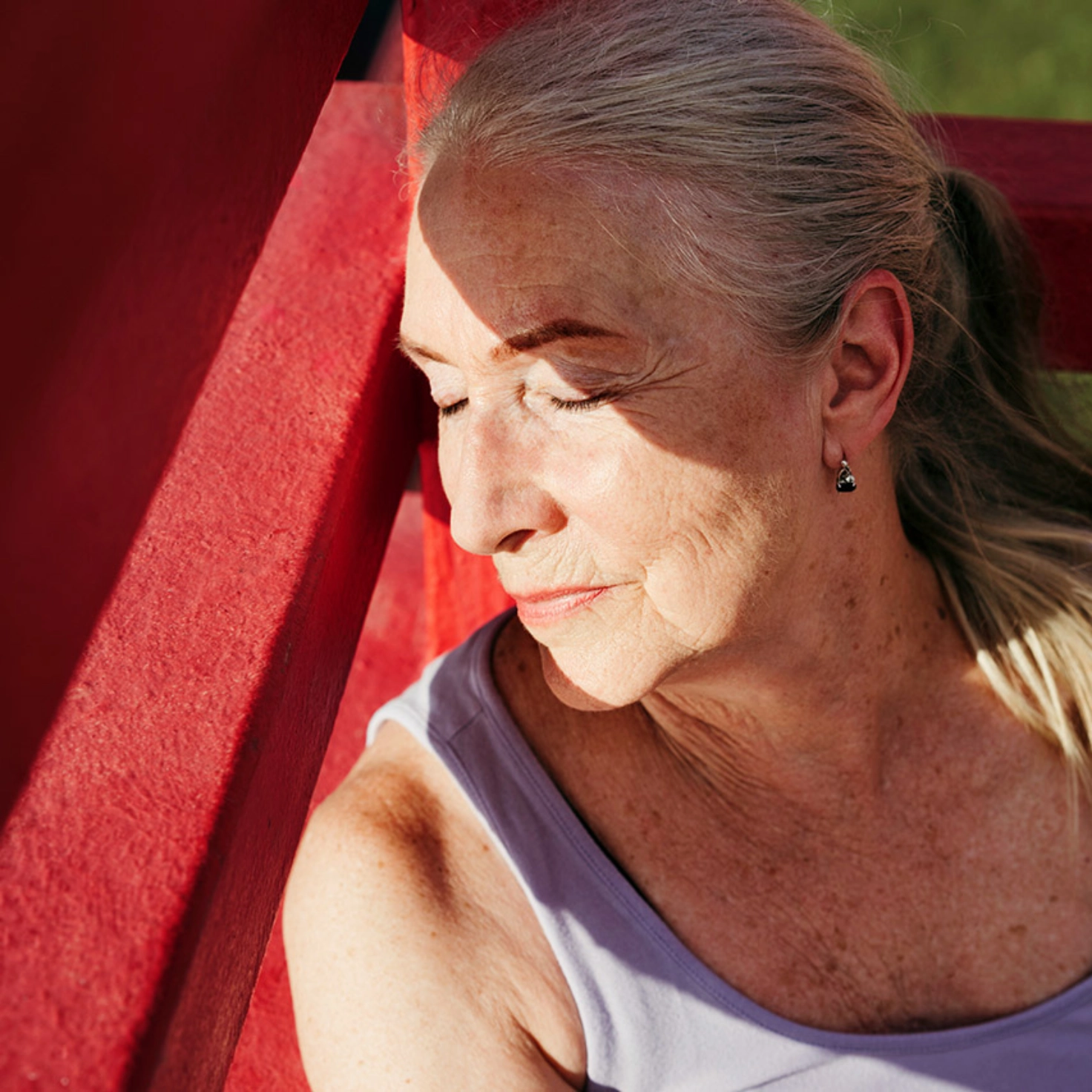 Eine Frau sitzt draussen und geniesst mit geschlossenen Augen die Sonne, die ihr halb ins Gesicht schein