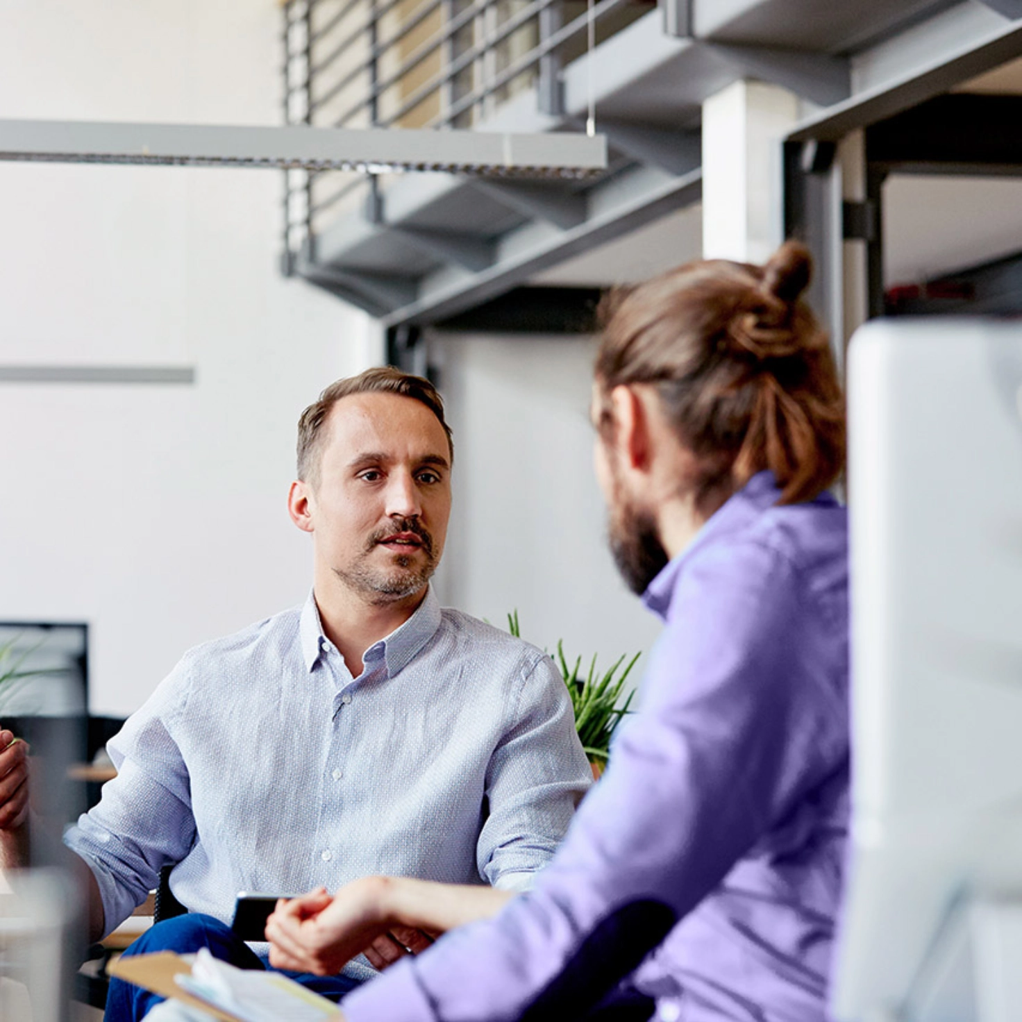 Zwei Männer sitzen nebeneinander am Arbeitsplatz und besprechen sich