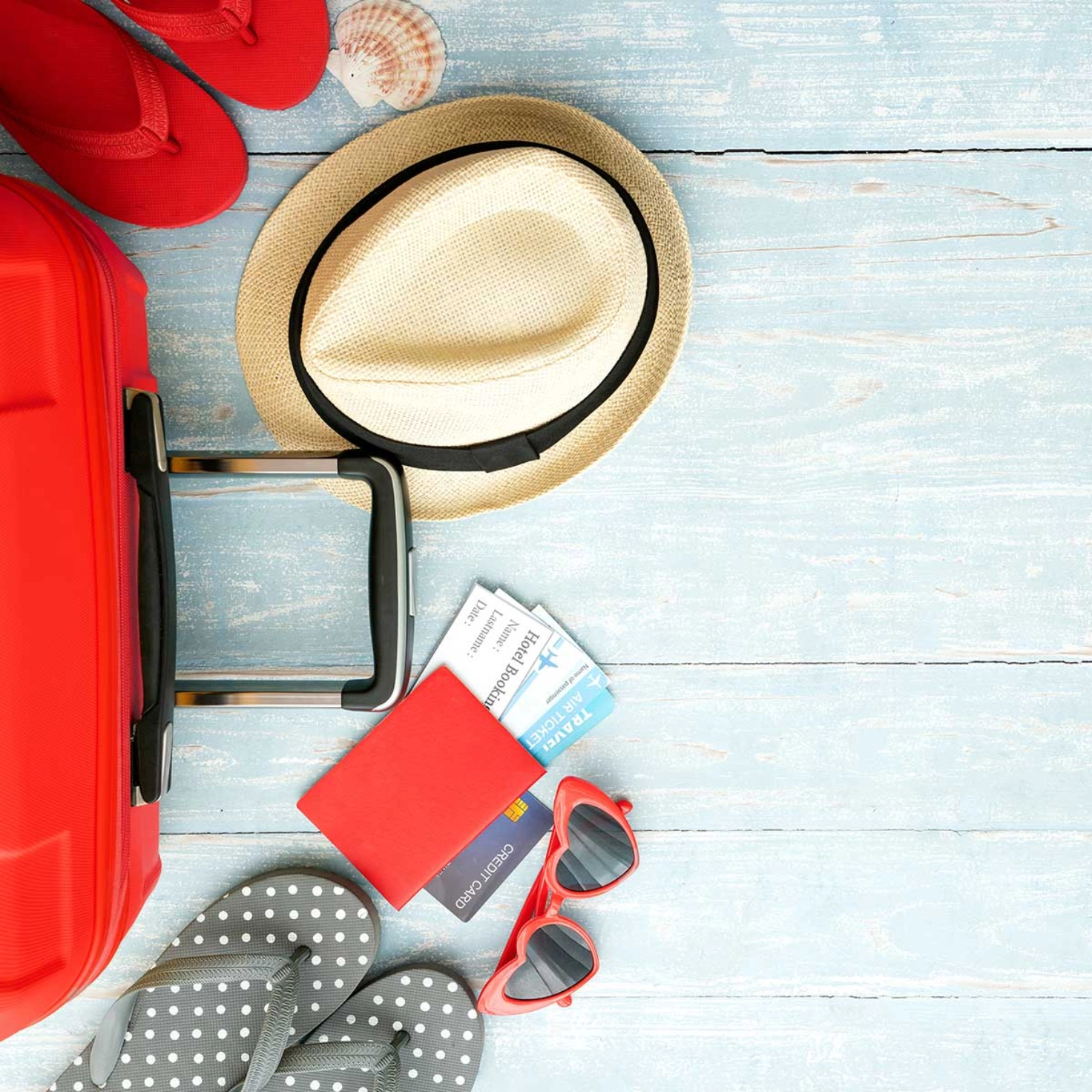 Una valigia a terra con accanto infradito, cappello e passaporto.