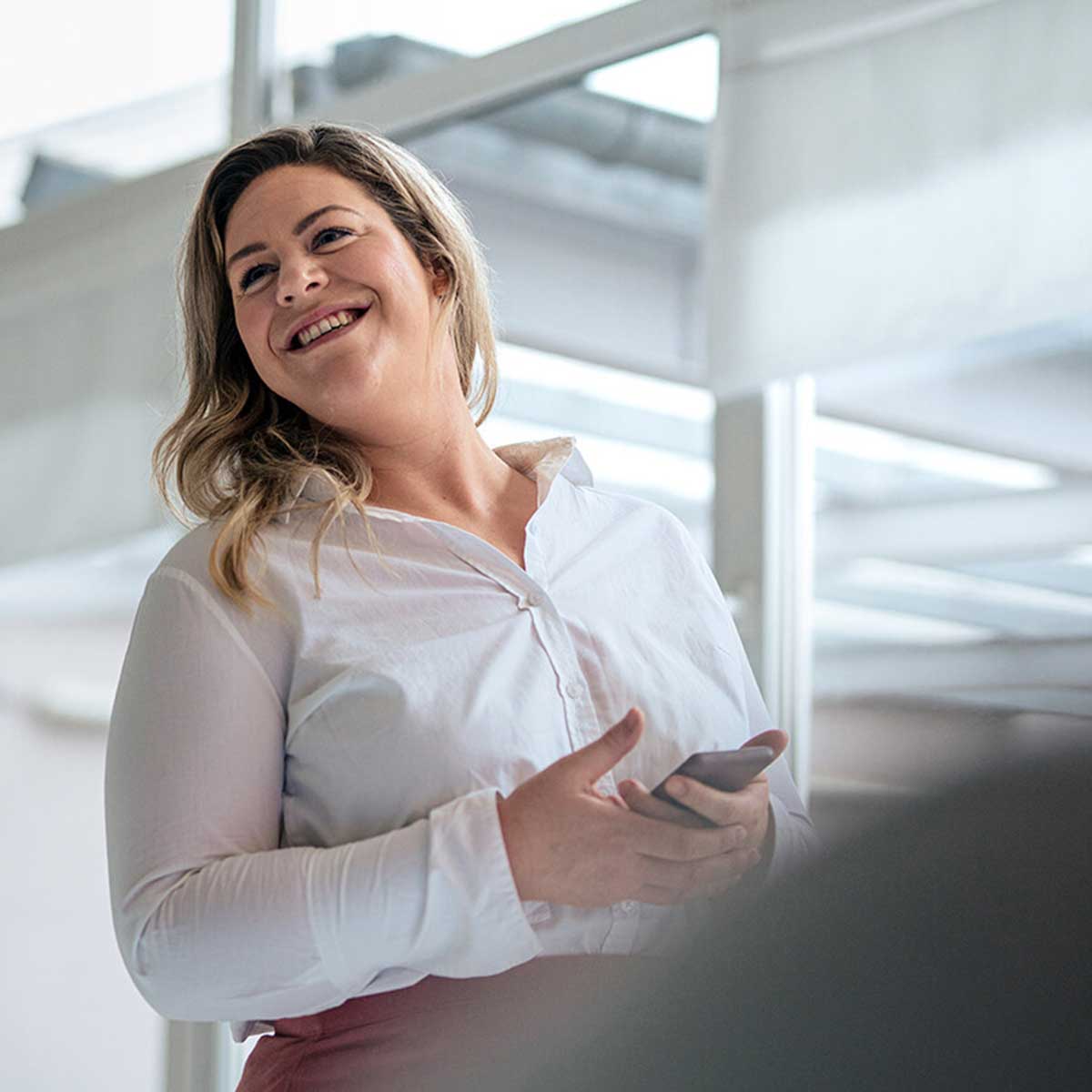 Eine lachende Frau hält ein Smartphone in der Hand