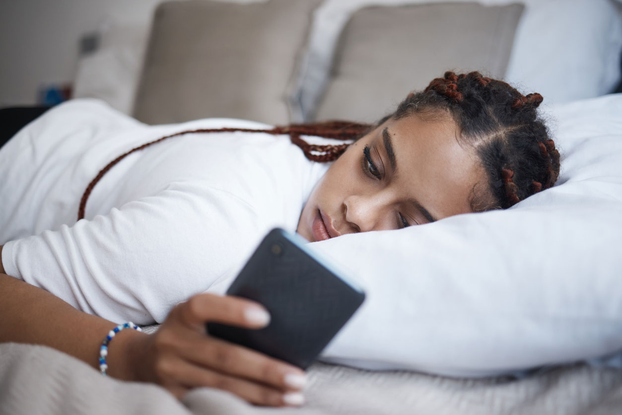 Jugendliche liegt auf dem Bett und schaut auf ihr Smartphone