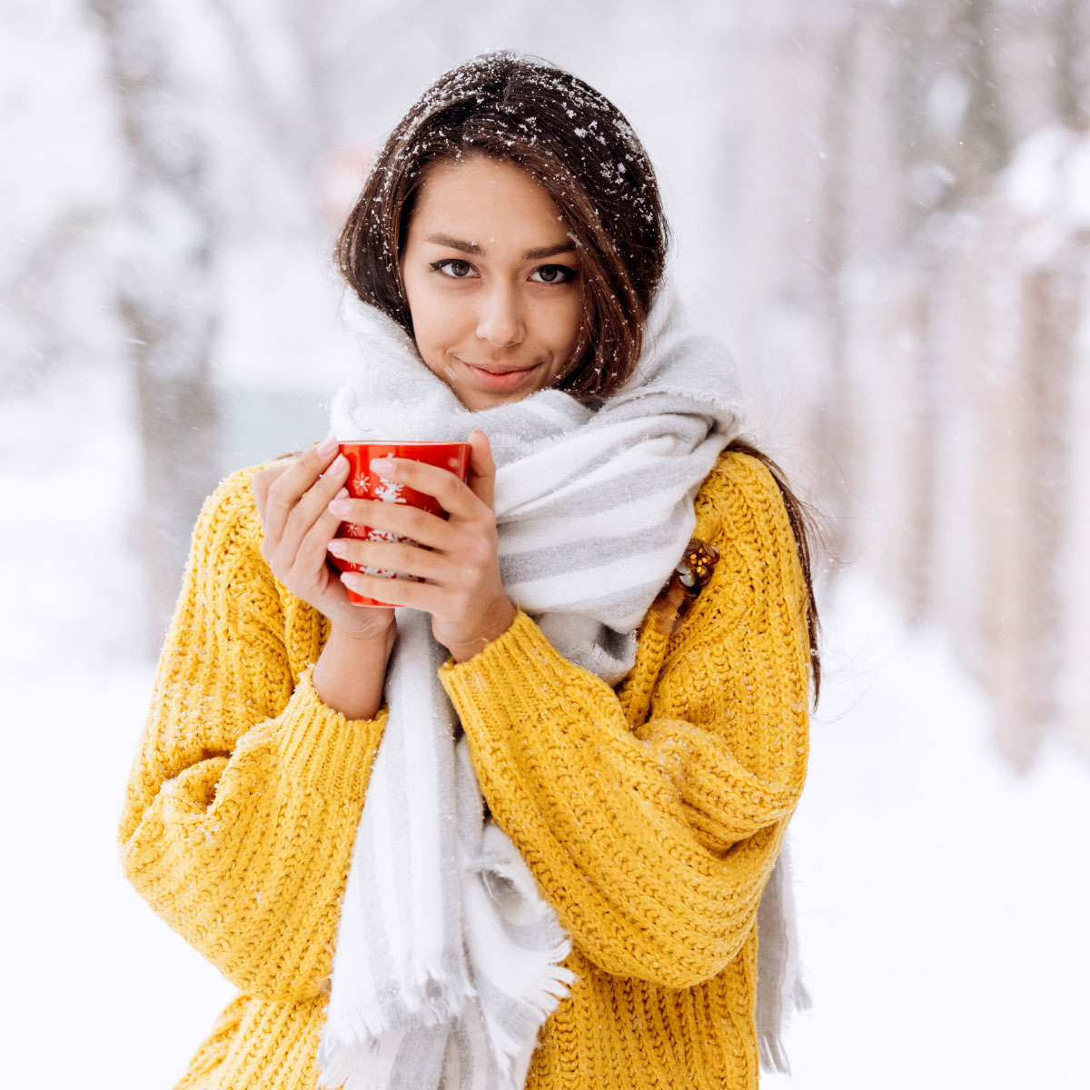 Frau steht in einer Winterlandschaft und hält eine Tasse mit Tee in der Hand